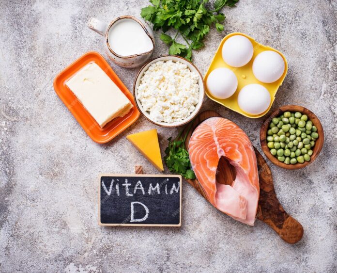 "Vitamin D-rich foods including salmon, eggs, dairy, and peas arranged on a rustic background with a chalkboard labeled 'Vitamin D.'"
