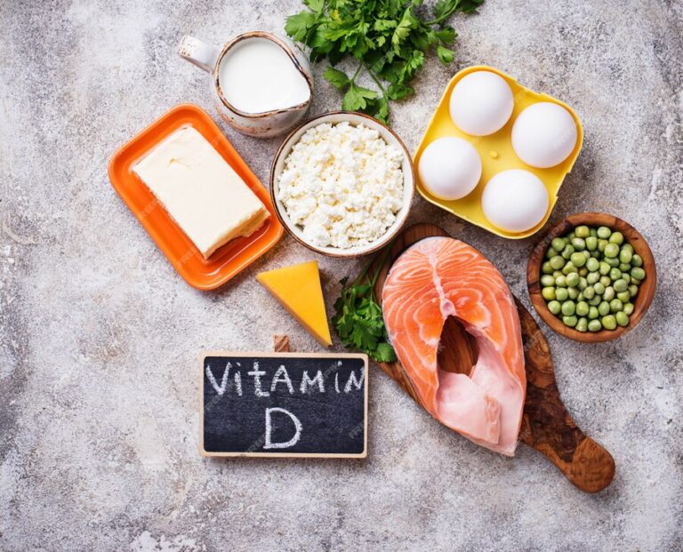 "Vitamin D-rich foods including salmon, eggs, dairy, and peas arranged on a rustic background with a chalkboard labeled 'Vitamin D.'"