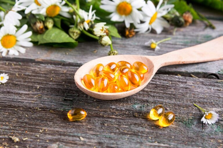 Vitamin E capsules in a wooden spoon on a rustic surface, surrounded by white daisies, symbolizing natural wellness