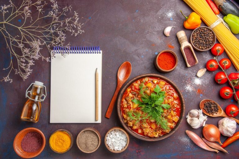 "Recipe Inspiration – A top-view composition featuring a bowl of delicious vegetable stew garnished with fresh herbs, surrounded by various spices, seasonings, and cooking ingredients. A blank notepad and pencil are placed nearby, perfect for jotting down creative recipe ideas."